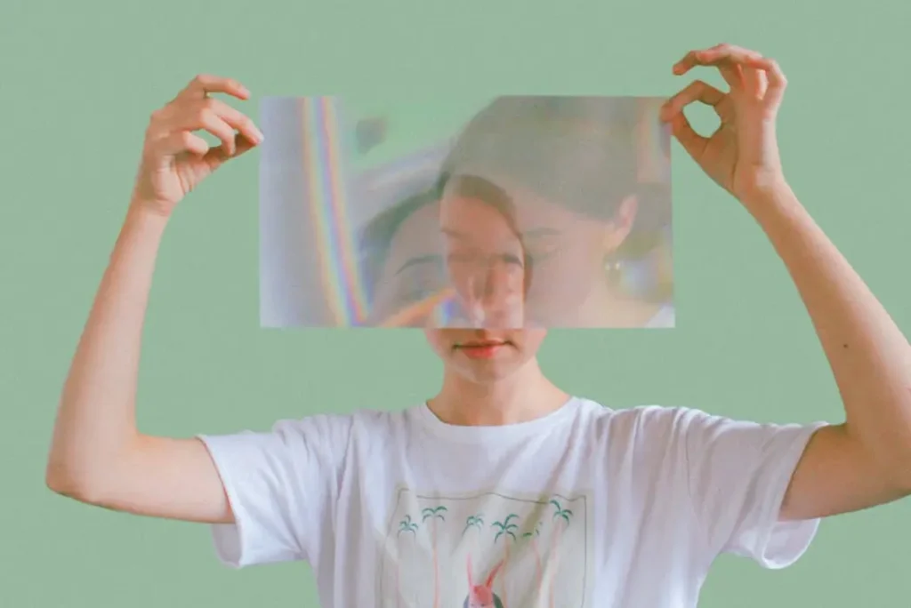 Woman holding a holographic prismatic sheet over her face wearing a graphic tee, symbolizing the unlimited color potential of sublimation printing.