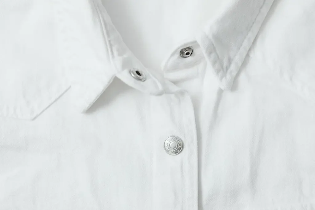 Close-up macro shot of a white cotton shirt collar with silver snap buttons, showing the thick double-knit weave of interlock fabric.