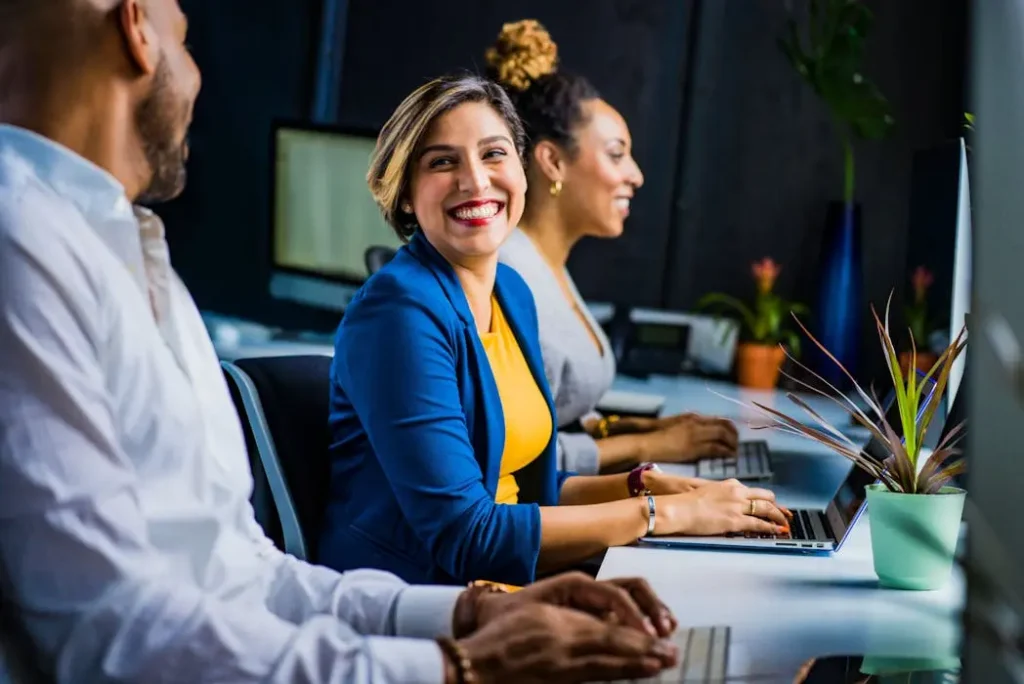 Smiling woman sitting at an office desk wearing a blue blazer and yellow top, representing a happy team with well-maintained uniforms.