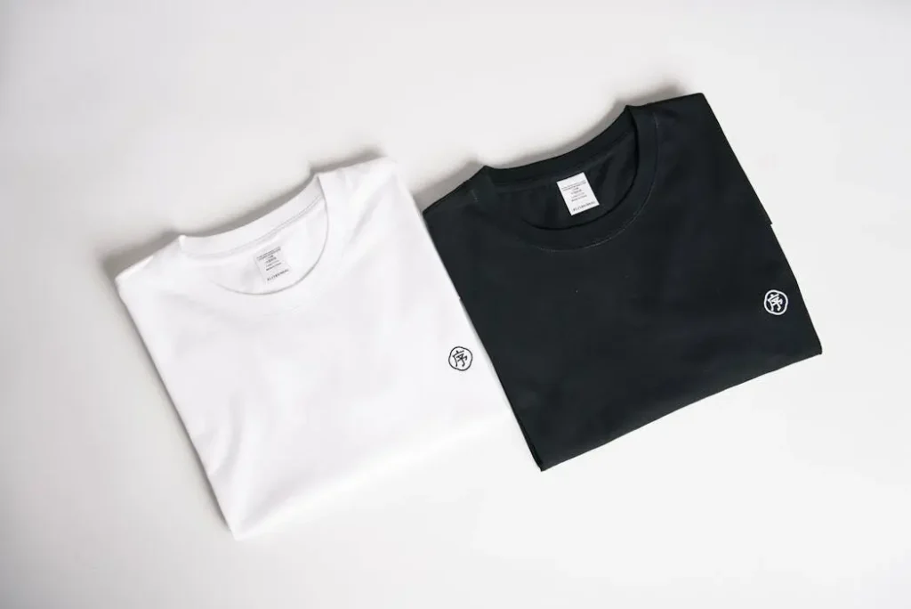Minimalist Logo Corporate T-Shirt Design - T-Shirt Printing KL | Custom Shirt Printing Malaysia White and black t-shirts featuring a small, discreet circular logo on the chest, representing modern minimalist corporate merchandise.