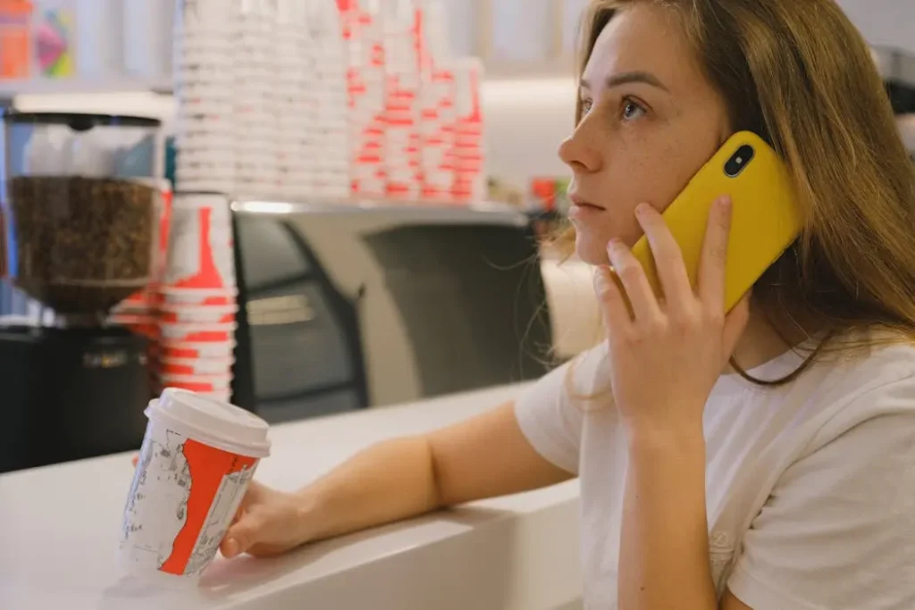 Young professional woman speaking on a mobile phone while holding a coffee cup, representing easy customer support for t-shirt printing orders.