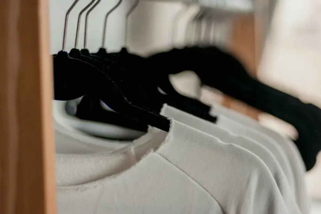 Close-up of a clothing rack filled with identical white t-shirts on black hangers, showing consistent manufacturing quality.