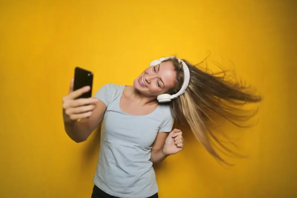 Happy woman with headphones dancing against a yellow background, wearing a grey t-shirt that allows for easy movement.