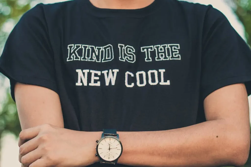 Close-up of a black t-shirt with sharp white text reading "kind is the new cool," demonstrating high-quality slogan printing.