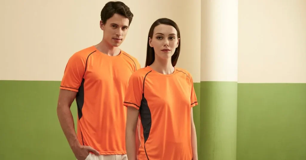 Male and female models wearing matching orange and grey dry-fit company uniforms, illustrating high-quality custom sportswear in Malaysia.