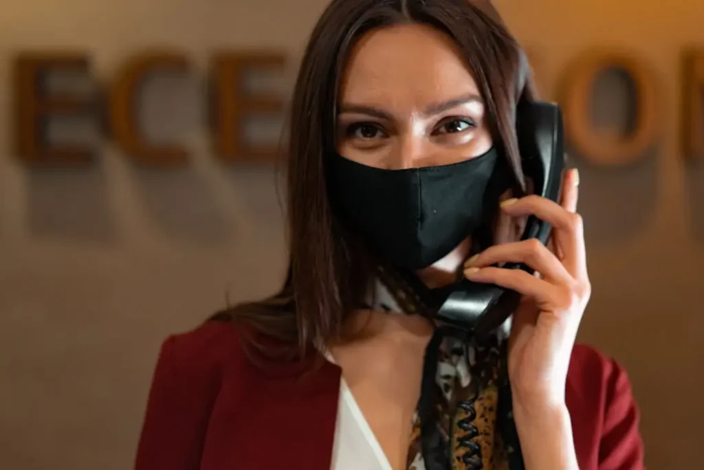 Professional receptionist wearing a maroon blazer and face mask answering a phone, representing consistent corporate identity.