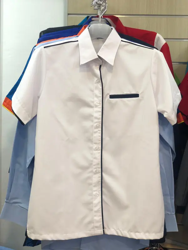White short-sleeve f1 corporate uniform shirt with black contrast piping on the pocket and placket, hanging on a display rack.