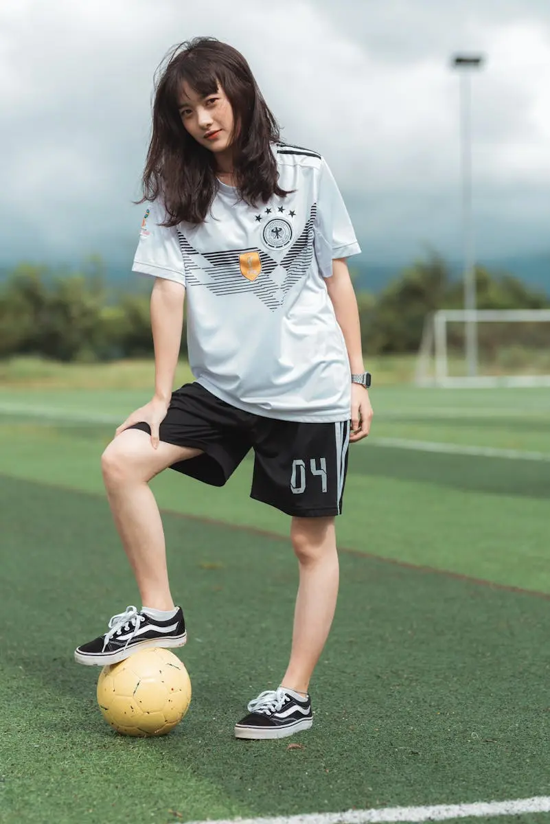 Young woman posing on a football pitch wearing a white custom sports jersey and black shorts, demonstrating the ladies' fit cutting.