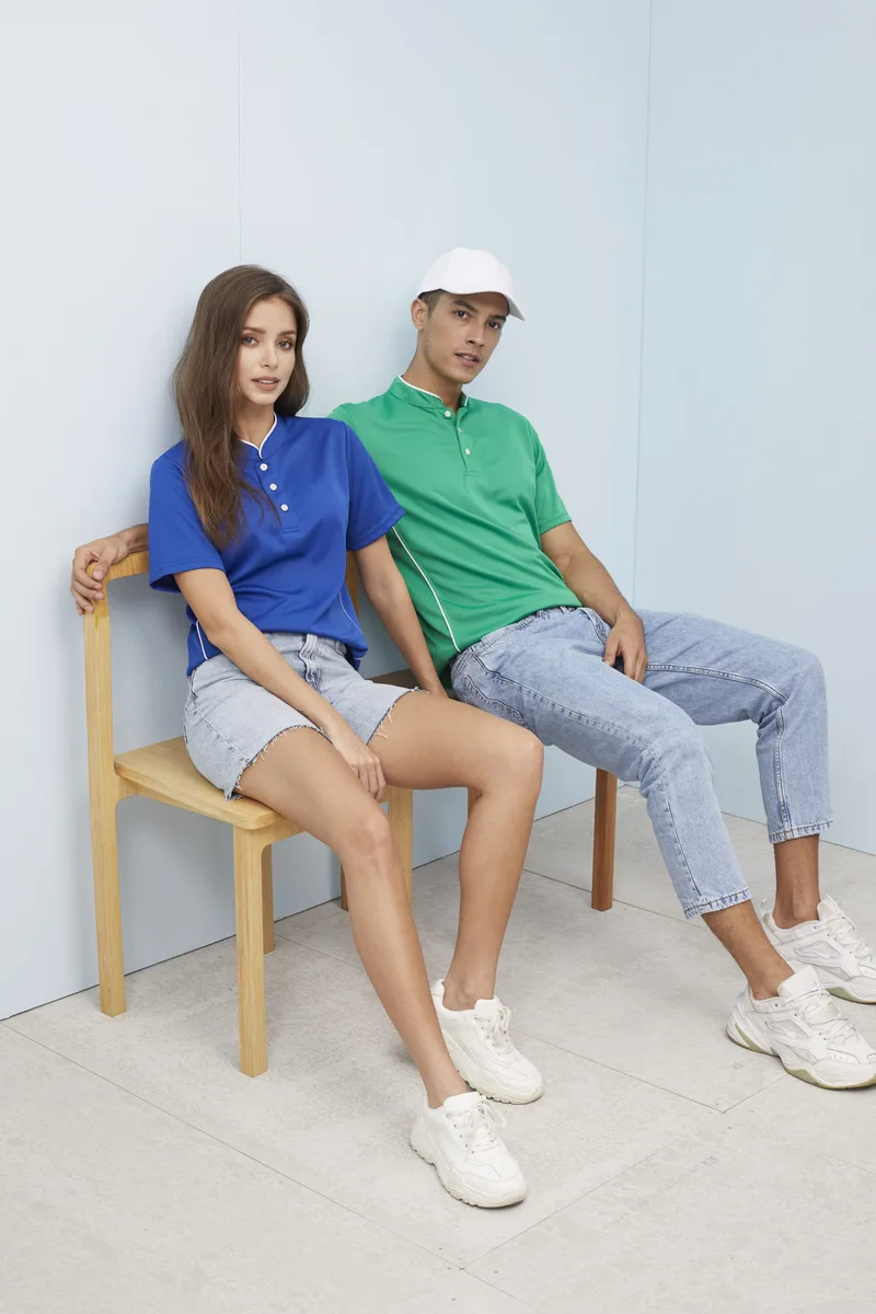 Young man and woman posing in studio wearing custom green and blue mandarin collar polo shirts with white piping trim, demonstrating male and female cuts.