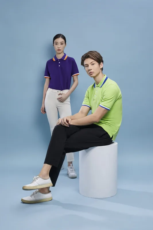 Young asian man and woman posing in studio wearing bright lime green and purple custom polo shirts with contrast collar trim.